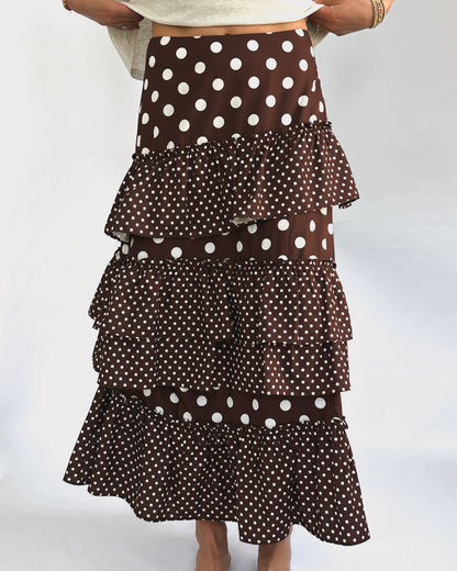 A stylish, brown layered skirt with white polka dots. The tiers vary in dot size, creating a playful and elegant look. Worn with bare feet.