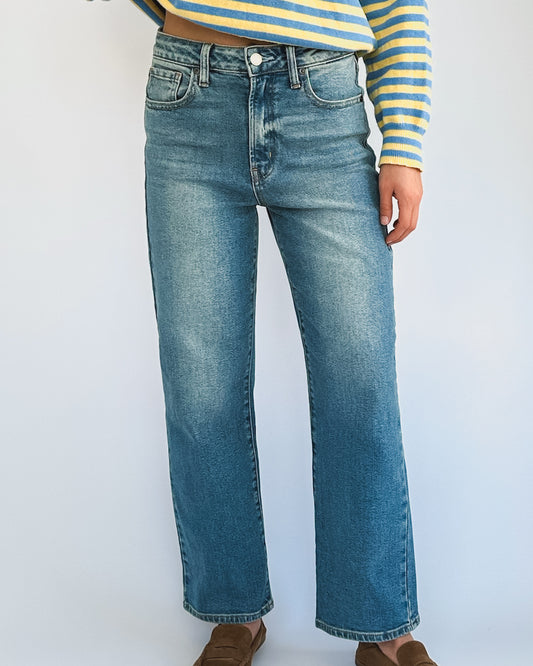 A person is wearing light blue denim jeans and a blue-and-yellow striped sweater, with hands resting by their sides. The tone is casual and stylish.