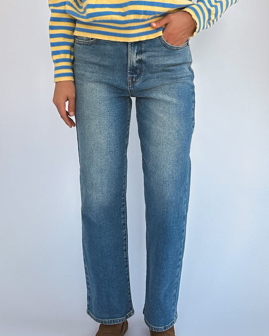 A person is wearing light blue denim jeans and a blue-and-yellow striped sweater, with hands resting by their sides. The tone is casual and stylish.