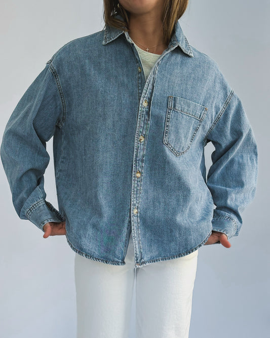 A person wearing a loose-fitting denim jacket, layered over a light-colored t-shirt and paired with white pants. The casual style suggests comfort and ease.