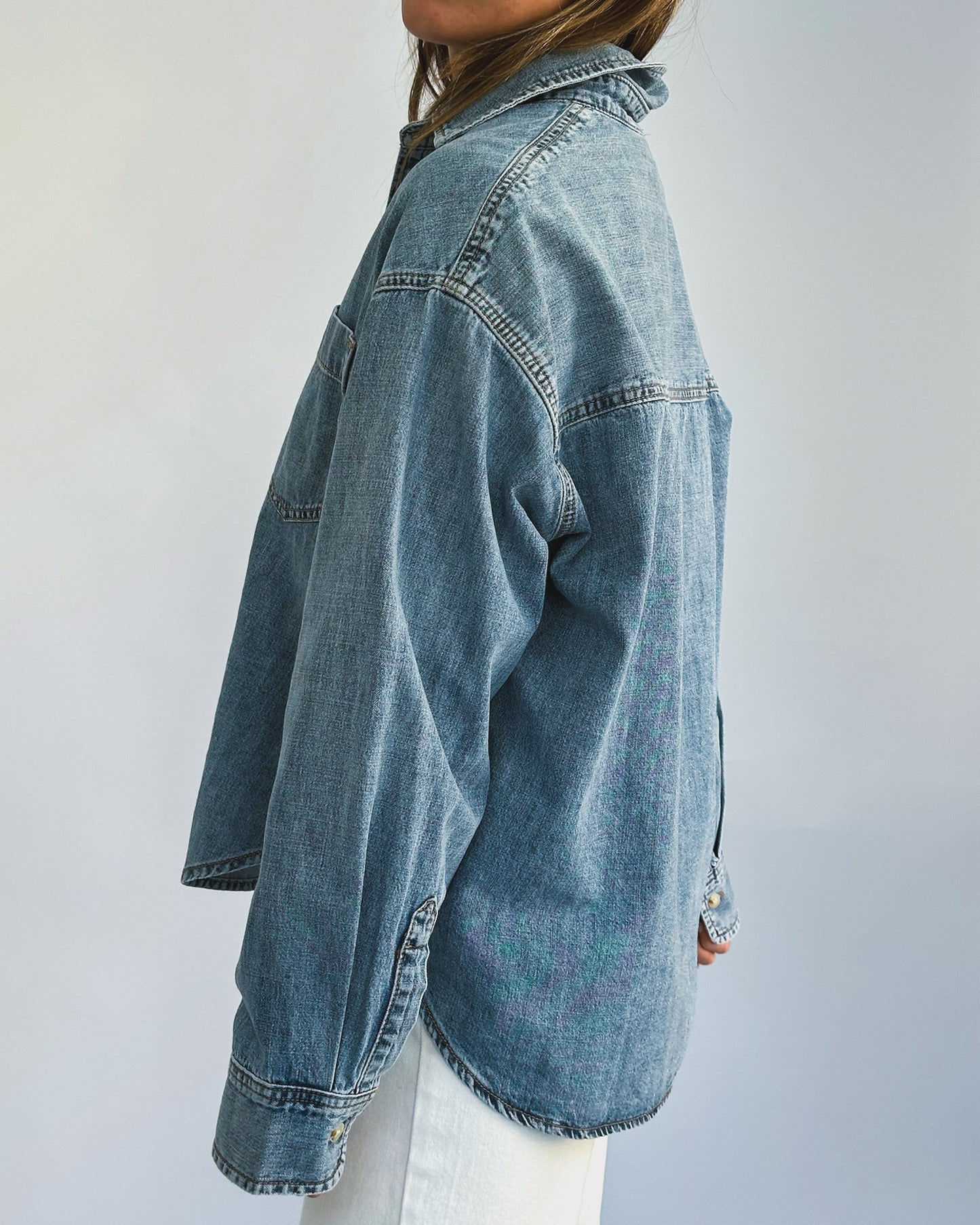 A person wearing a loose-fitting denim jacket, layered over a light-colored t-shirt and paired with white pants. The casual style suggests comfort and ease.