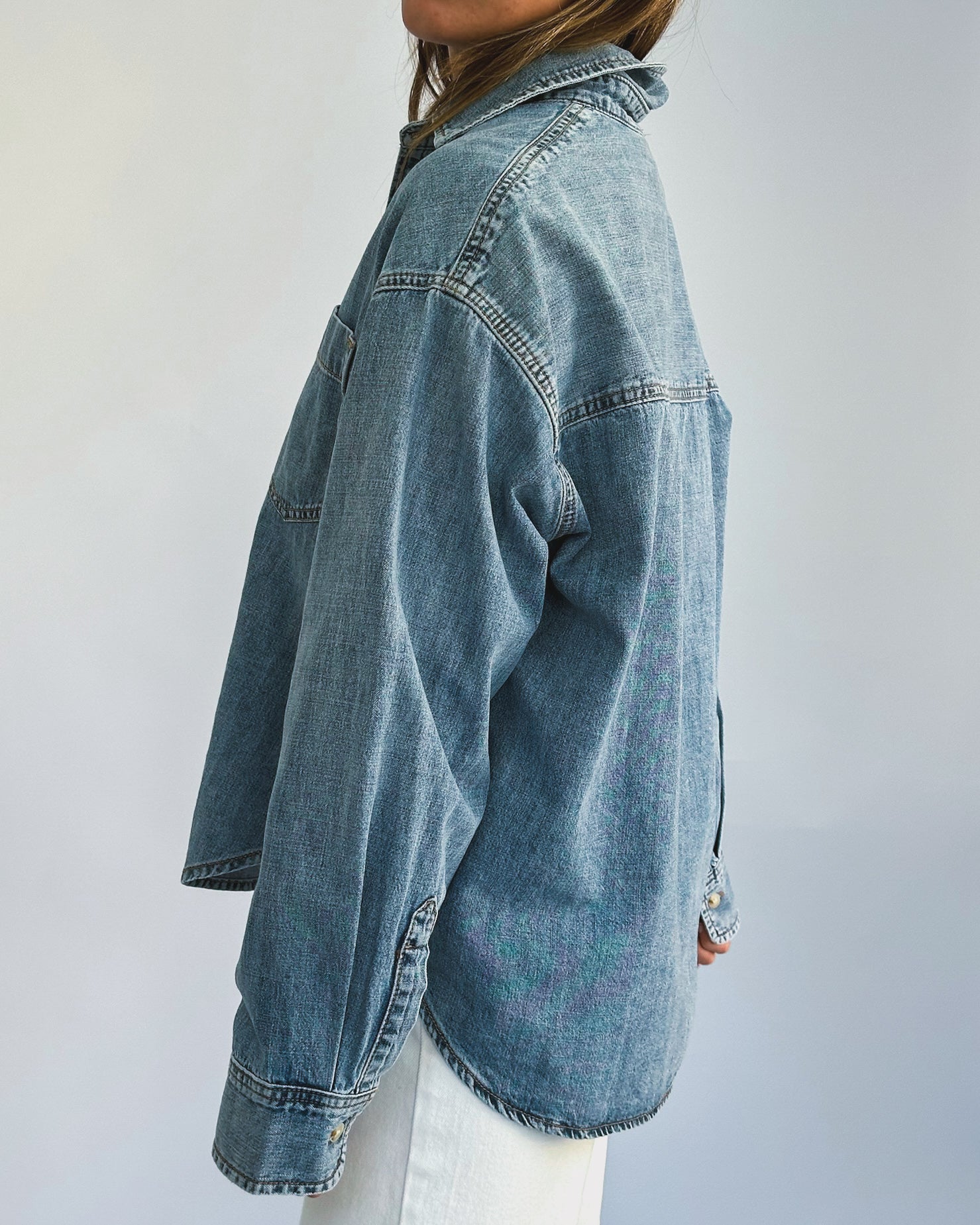 A person wearing a loose-fitting denim jacket, layered over a light-colored t-shirt and paired with white pants. The casual style suggests comfort and ease.