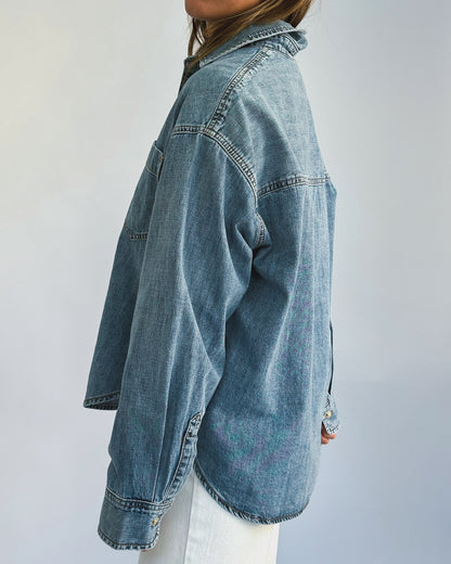 A person wearing a loose-fitting denim jacket, layered over a light-colored t-shirt and paired with white pants. The casual style suggests comfort and ease.