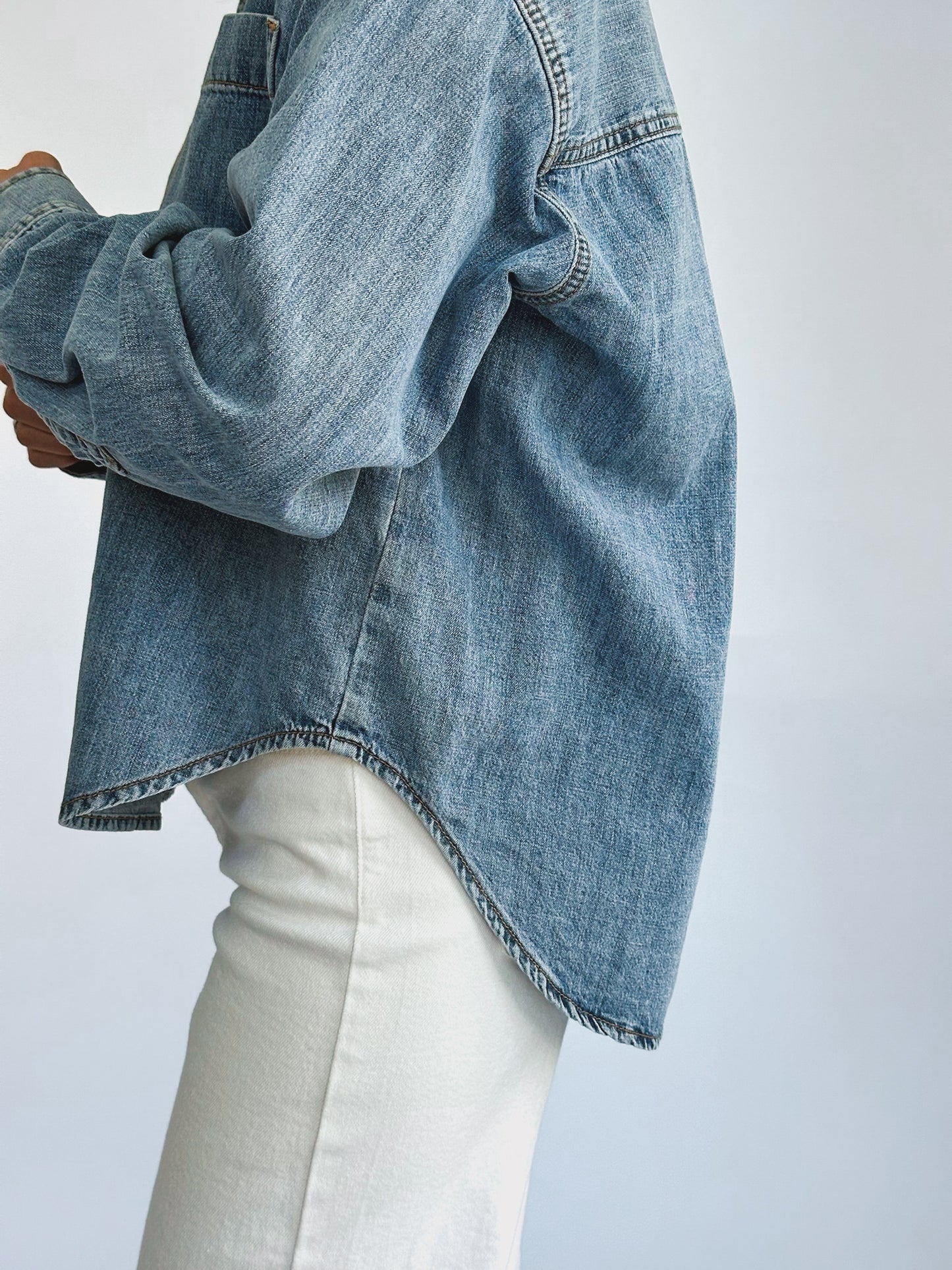 A person wearing a loose-fitting denim jacket, layered over a light-colored t-shirt and paired with white pants. The casual style suggests comfort and ease.