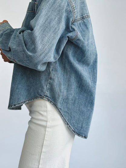 A person wearing a loose-fitting denim jacket, layered over a light-colored t-shirt and paired with white pants. The casual style suggests comfort and ease.