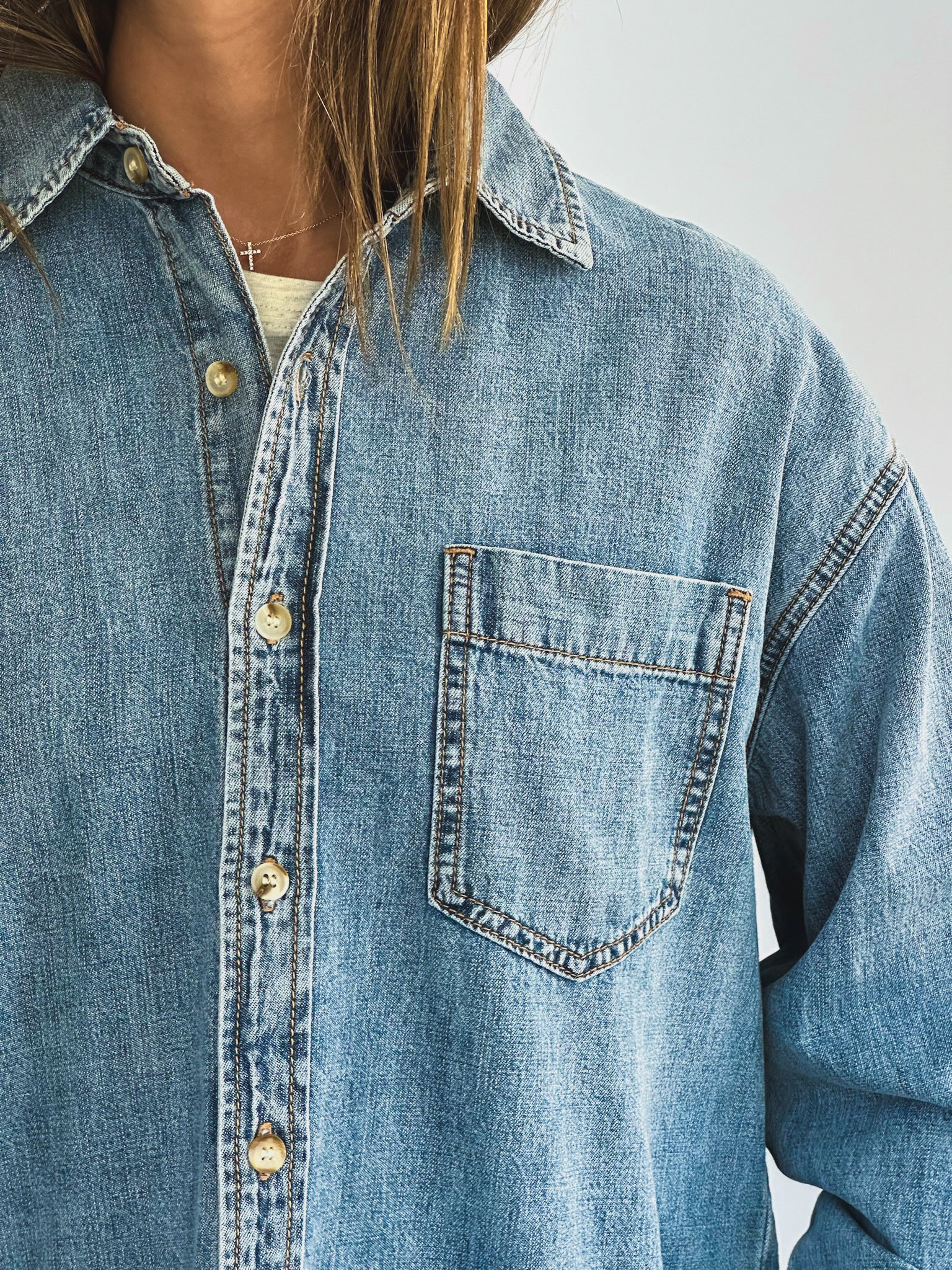 A person wearing a loose-fitting denim jacket, layered over a light-colored t-shirt and paired with white pants. The casual style suggests comfort and ease.